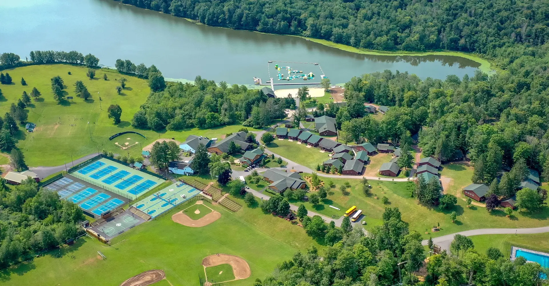 Lago de un campamento de verano con jóvenes nadando, muelles de madera y montañas al fondo